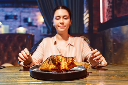 Lunch at the restaurant. A young woman holds cutlery in her hands to eat fried fish. low angle view. Dish close-up. nutrition and diet.の写真素材
