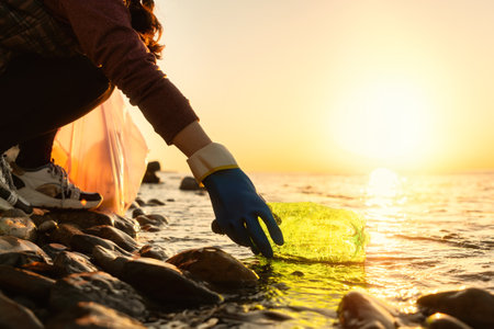 Coastal cleanup and garbage collection for recycling. A woman volunteer collects plastic bottle by the sea or river, closeup of hand. low angle view. World environment day and Earth day concept.の写真素材