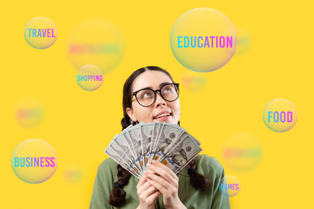 save money. Pretty smiling caucasian young woman wearing eyeglasses holding fan of dollar currency and dreaming about life purposes. Concept of shopping, investment and advertising.の写真素材