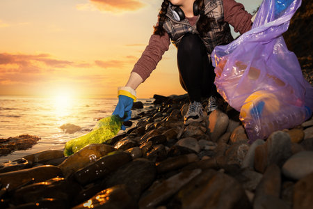 A female volunteer collects garbage on the ocean. Cleaning of the coastal zone and preservation of ecology. Trash collection for recycling. Concept of Earth Day.の写真素材