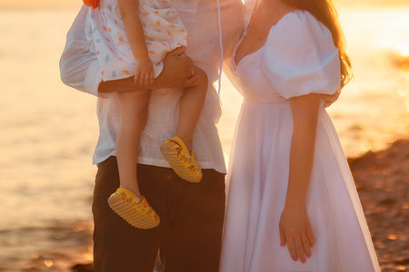 Adoption of children. Young happy couple with child. Sea and sunset background. Mother and father are holding little daughter in their arms. Concept of family planning.の写真素材