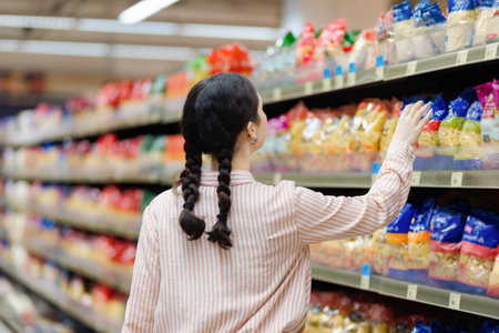 Young housewife takes food from shelve. Showcase at background. back view. Concept of shopping in supermarket and consumerism.の写真素材