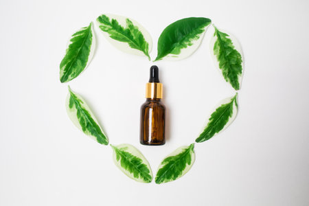 A brown glass bottle with essential oil for face care on a white background with heart of leaves. flat lay. organic cosmetic products.の写真素材