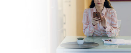 Web banner of freelance and remote work. Young beautiful Caucasian woman is sitting at table and using smartphone. Mock up. Concept of social networks and Internet search.の写真素材