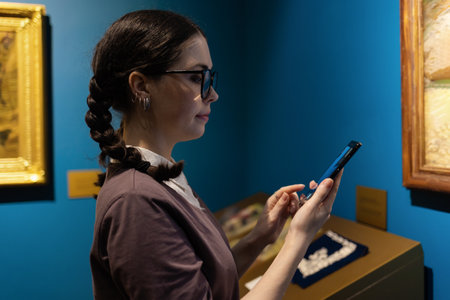 modern museum exhibition. Side view of young Caucasian woman uses smartphone. In background are arts. Concept of art visiting gallery.の写真素材