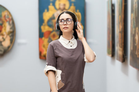 Portrait of young Caucasian pretty woman wearing headphones and contemplates ancient artefacts. Student arts visiting exhibition. Concept of education and culture.の写真素材