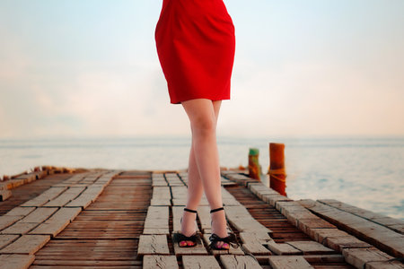 Elegant female legs in tights, heeled sandals and a red skirt on the pier, close-up. Sea and sky in the background. The concept of epilation, weight loss and hair removal.の写真素材