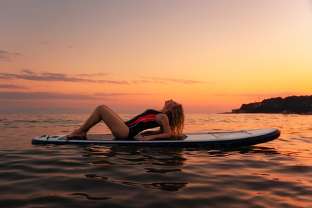 Silhouette of young woman posing lying at sup board in the ocean. copyspace. Sunset at the background. The concept of summertime, sport and vacation.の写真素材