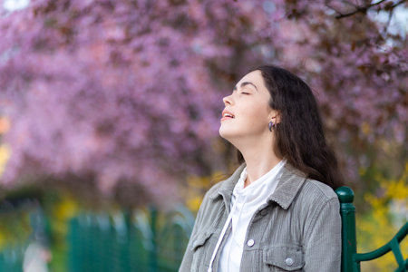 springtime. Portrait of young smiling Caucasian woman smelling fragrance of blooming tree in background. Concept of carefree and psychology.の写真素材