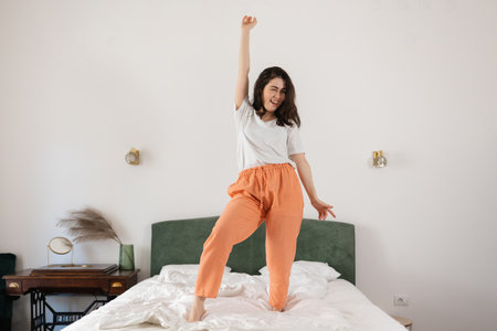 Happy young Caucasian woman enjoying and dancing on bed in bedroom. Enjoying winning.の写真素材