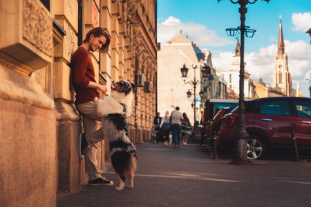 Side view of young Caucasian man with pure breed aussie dog poses leans wall. Background of the city. Friendship with pet.の写真素材