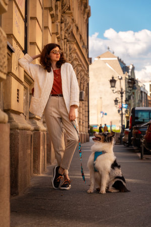 Friendship with pet. Side view of young pretty Caucasian woman with pure breed aussie dog poses leans wall. vertical orientation.の写真素材