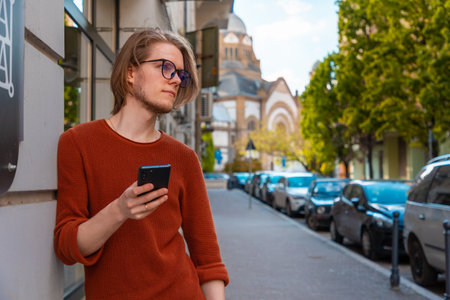 Portrait of handsome young Caucasian man holding smartphone. summer street background.の写真素材