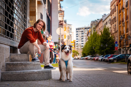 Friendship with pet. Young handsome Caucasian man sitting on steps posing with pure breed aussie dog.の写真素材