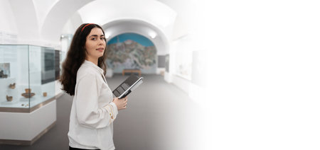 Web banner of educational excursion. Young caucasian woman holds brochure visiting museum. light hall background. Mock up and copy space. Concept of cultural exhibition.の写真素材