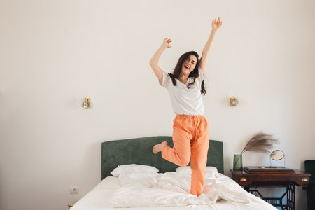 Happy young Caucasian woman dancing on bed in bedroom. Freedom and winning.の写真素材