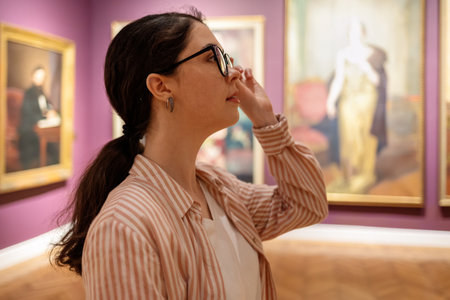 Side view of young Caucasian woman wearing glasses and looking at exhibition. Masterpieces in background. Concept of Museum Day and cultural education.の写真素材