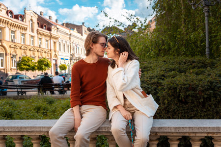 Young Caucasian couple relax in park sitting on ballustrade. Romantic date in Valentine's Day.の写真素材