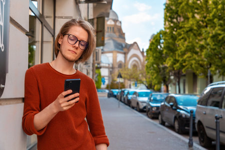 Portrait of handsome young Caucasian man holds smartphone and reads message. summer street background.の写真素材
