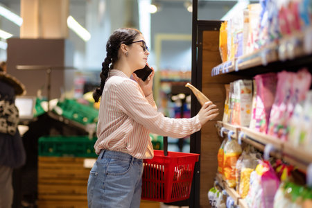 shopping. Pretty caucasian woman choosing food in supermarket and talking on smartphone. side view.の写真素材