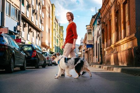 Young handsome Caucasian man wearing eyeglasses calls in cellphone walking with leashed pure breed aussie dog. beautiful city landscape backgroundの写真素材