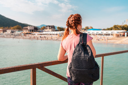 A woman with a backpack admires the ocean and the beach. The view from the back. The concept of freedom and travel.の写真素材