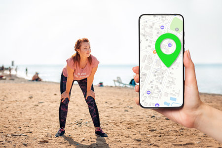 An adult tired woman in sportswear takes a break during a workout. A female's hand holding a smartphone with an online map. sport and gps navigation.の写真素材