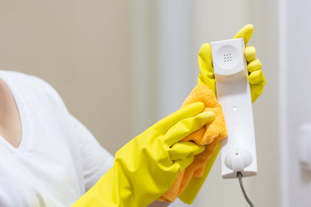 Cleaning lady in yellow rubber gloves wipes telephone receiver. Hands close-up. Cleaning and...