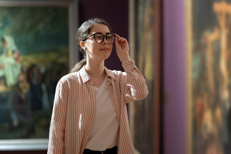 Portrait of young pretty Caucasian woman carefully looking at picture. Masterpieces in background....