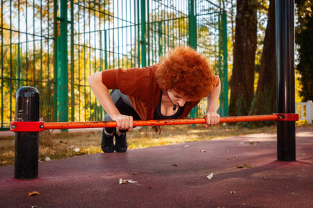 Training in city park. Caucasian adult woman does push-up from horizontal bar. Concept of fitness and aerobics.の写真素材