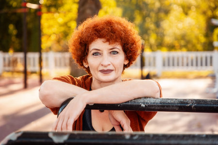 Portrait of adult Caucasian woman with makeup and ginger curly hair posing in sports park. Concept of healthy lifestyle.の写真素材