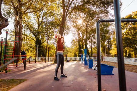Healthy lifestyle. Mid adult happy Caucasian ginger hair woman is doing sports using dumbbells. Copy space. Fitness and aerobic at city park.の写真素材