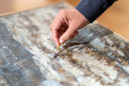 Restorer artist restore paint on picture. Close-up of hand holds brush. Selective focus.の写真素材