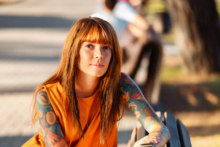 Portrait of young pretty Caucasian woman with tattoos poses sitting on bench. Concept of psychology.の写真素材