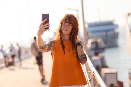 Online communication. Pretty young woman with tattoos holds cellphone and take selfie. Freedom and...