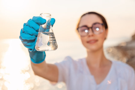 Defocused portrait of smiling ecologist wearing protective gloves and eyeglasses, holds test sample flask of pure water. Concept of recycle resources and ecology.の写真素材