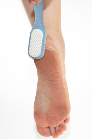 Close up of female leg with pumice rubbing peeling skin of soles on heels. White background. Vertical orientation. Skin care and pedicure.の写真素材
