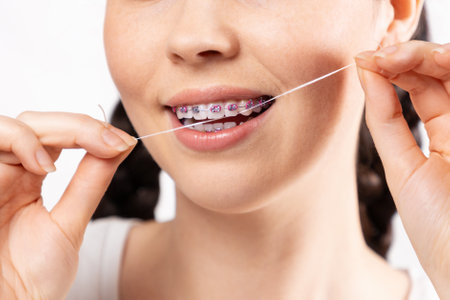 Close up of young Caucasian woman with brackets on teeth cleaning interdental space using orthodontic floss. White background. Concept of dental care during orthodontic treatment.の写真素材