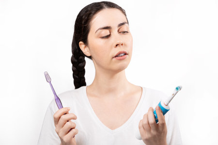 Portrait of young Caucasian woman with ligature braces on her teeth, choosing between an electric and manual toothbrush. Concept of orthodontic treatment and dental care.の写真素材