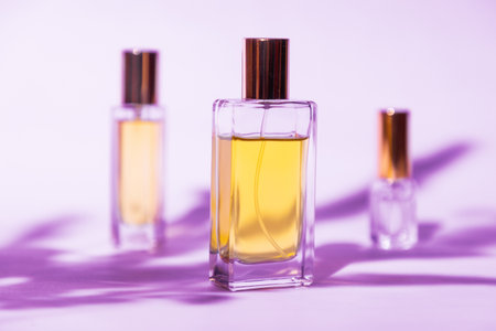 Three glass transparent rectangular bottles of golden perfume on lilac background with sunlight and shadows of leaves. Minimal style perfumery template.の写真素材