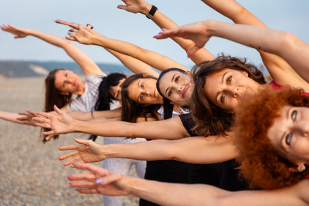 Outdoor fitness. Portrait of row of smiling beautiful young Caucasian women training on beach. Yoga...