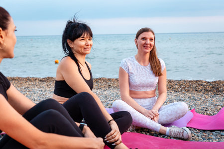Yoga class. Group of happy young-adult multi-racial women are sitting on sports mats on wild beach and talking to each other. Concept of female circle of communication.の写真素材