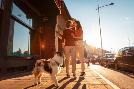 Happy romantic couple walking on the street with purebred dog Aussie. Pet training. Friendship with pet. Sunset light in background.の写真素材