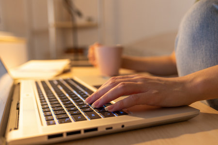 Close up of laptop on desk in home office. Female hands types on keyboard. Concept of remote work,...