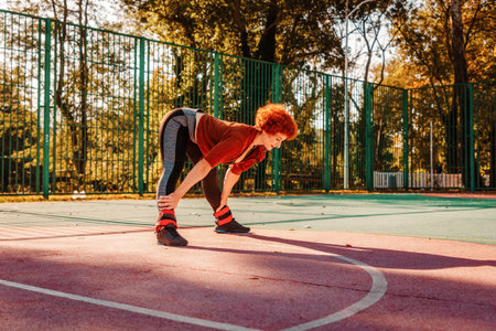 Tired adult woman in sportswear training on playground. Copy space. Sunlight in background. Concept...