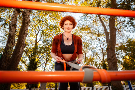 Bottom view through horizontal bar of mid adult Caucasian woman training with sports elastic band...