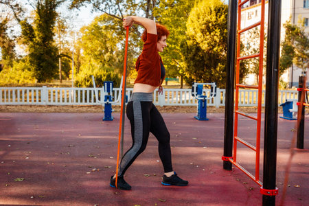 Side view of mid adult Caucasian woman wearing sportswear training with sports elastic band. Autumn...
