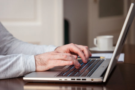 Side view of male hands writing with pen on paper and using laptop. Modern remote work and business....