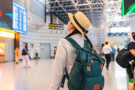Young Caucasian woman in a straw hat, carrying a backpack, walks through the airport. Rear view, from the back. Traveling by plane, check-in for a flight.の写真素材
