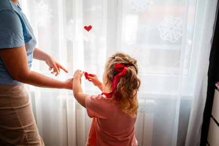 Mother and her daughter decorate the curtains on the window with red paper hearts. A celebration for Valentine's Day and Mother's Day.の写真素材
